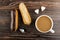 Eclairs with chocolate and peanut, pieces of sugar, spoon, coffee with milk in cup on wooden table. Top view