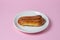 Eclairs on a pink background. One eclair on a white plate.