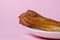 Eclairs on a pink background. One eclair on a white plate.