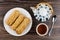 Eclairs in plate, teapot, spoon, cup of tea on table