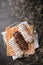 Eclairs or profiteroles with black chocolate and white chocolate with custard inside on a metal plate on a dark background.