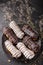 Eclairs or profiteroles with black chocolate and white chocolate with custard inside on a metal plate on a dark background.