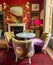 Eclectic living room with brightly coloured velvet upholstered chairs, pink lampshade and deep red patterned carpet.