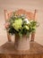 Eco friendly composition with flowers bouquet in DIY cardboard vase standing on old wooden chair on beige background