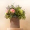 Eco friendly composition with flowers bouquet in DIY cardboard vase standing on wooden round stand on beige background