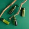 Eco friendly cosmetic products set on green background. Top view green glass bottles and wooden branch. Natural organic beauty