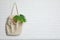 Eco tote bag with leaf hanging on white brick wall.