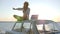 Eco-tourism, girl sits on car roof in backlight talking on cellphone and holds solar array, young woman using powered