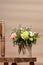 Ecological holiday geometric composition with flowers bouquet in DIY cardboard vase and old wooden chair on beige