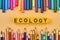 ECOLOGY inscription on yellow blocks and colored school supplies background.