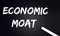 ECONOMIC MOAT Text on Black Chalkboard with a piece of chalk