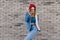 Ecstatic blonde girl in red hat standing in confident pose beside brick wall. Outdoor shot of cute