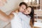 Ecstatic woman with brown eyes huggs with boyfriend while he making selfie. Indoor photo of caucasian brunette guy