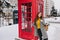 Ecstatic woman in trendy yellow sweater posing with pleasure next to red phone booth in winter. Outdoor photo of relaxed