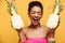 Ecstatic young woman with afro hairstyle and colorful makeup holding two halves of fresh appetizing pineapple isolated, over yell