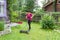Ederly woman mowing grass with lawn mower in the garden