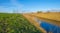 Edge of a canal in a green grassy landscape in wetland in sunlight under a blue sky in winter