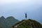 At the edge of the cliff there is a small lawn with the rocks. The tourist girl jumps full of happiness. The high mountains.