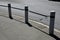 At the edge of the sidewalk is granite pillars connected by hanging rods similar to a chain. Cylindrical pillars protect pedestria