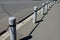 At the edge of the sidewalk is granite pillars connected by hanging rods similar to a chain. Cylindrical pillars protect pedestria