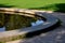 Edge of a stone sandstone circular fountain in the park. built of sandstone filled with water. lined with a light threshing gravel
