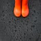 The edges of the orange rain boots are on a wet wet surface covered with raindrops.
