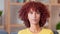 Edgy young woman with a curly red afro smiling while sitting in her living room at home. Happy female feeling positive