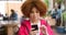 Edgy young woman with red afro using her phone while out in the city. Trendy female sending a text, browsing the