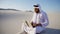 Educated male Muslim Arabian UAE Sheikh architect sits with gadg