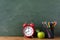 Education and back to school template with alarm clock, green apple and colorful pencils against blackboard.