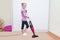 Education of children concept, cleaning. Young blond girl cleaning carpet in her room with vacuum cleaner