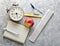 Education equipment. Alarm clock, notepad, ruler, apple, pen, compasses on a gray concrete background. Top view, flat lay style.