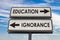 Education versus ignorance road sign with two arrows on blue and grey sky background. White two street sign with arrows on metal