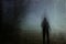 An eerie silhouette of a lone hooded figure in a field on a winters night. With a dark, spooky blurred abstract, grunge effect edi