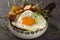 Egg with fries and fried salami in a rustic pan with herbs