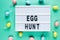 Egg hunt text on lightbox on green pastel paper background with yellow, pink, blue eggs Bright template for Easter, top view,