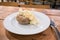 Egg Mayonnaise filling on a baked jacket potatoe on white plate with cutlery on a wooden table in a cafe