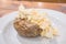 Egg Mayonnaise filling on a baked jacket potatoe on white plate with cutlery on a wooden table in a cafe