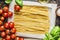 Egg Noodles in wrapping paper and fresh cooking ingredients: basil and tomatoes, top view