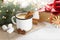 Eggnog with cinnamon, anise and nutmeg in a white mug on a wooden table near the branches of a Christmas tree and decorative toys