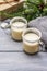 Eggnog cocktail in two glasses mug arranged with christmas decoration on light wooden table. Evergreen fir tree branch, gift, cozy