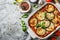 Eggplant casserole with cheese and tomato sauce in a white baking dish on a gray background with ingredients for cooking.