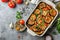 Eggplant casserole with cheese and tomato sauce in a white baking dish on a gray background with ingredients for cooking.