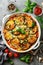 Eggplant casserole with cheese and tomato sauce in a white baking dish on a gray background with ingredients for cooking.