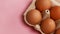 Eggs in basket. Open egg box with brown eggs on pink background. Healthy food and organic protein breakfast concept