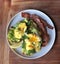 Eggs Benedict. Top view. Poached egg on white toasted bread with smashed avocado, rocket, bacon, Hollandaise sauce and