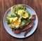 Eggs Benedict. Top view. Poached egg on white toasted bread with smashed avocado, rocket, bacon, Hollandaise sauce and