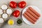 Eggs in carton, tomatoes, salt, bowl with parsley, plate with sausages on wooden table. Top view