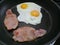 Eggs frying sunny side up with two strips of bacon