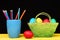 Eggs and pencils. Coloured crayons in blue mug and Easter decorations in green basket and red egg lying on yellow wooden
